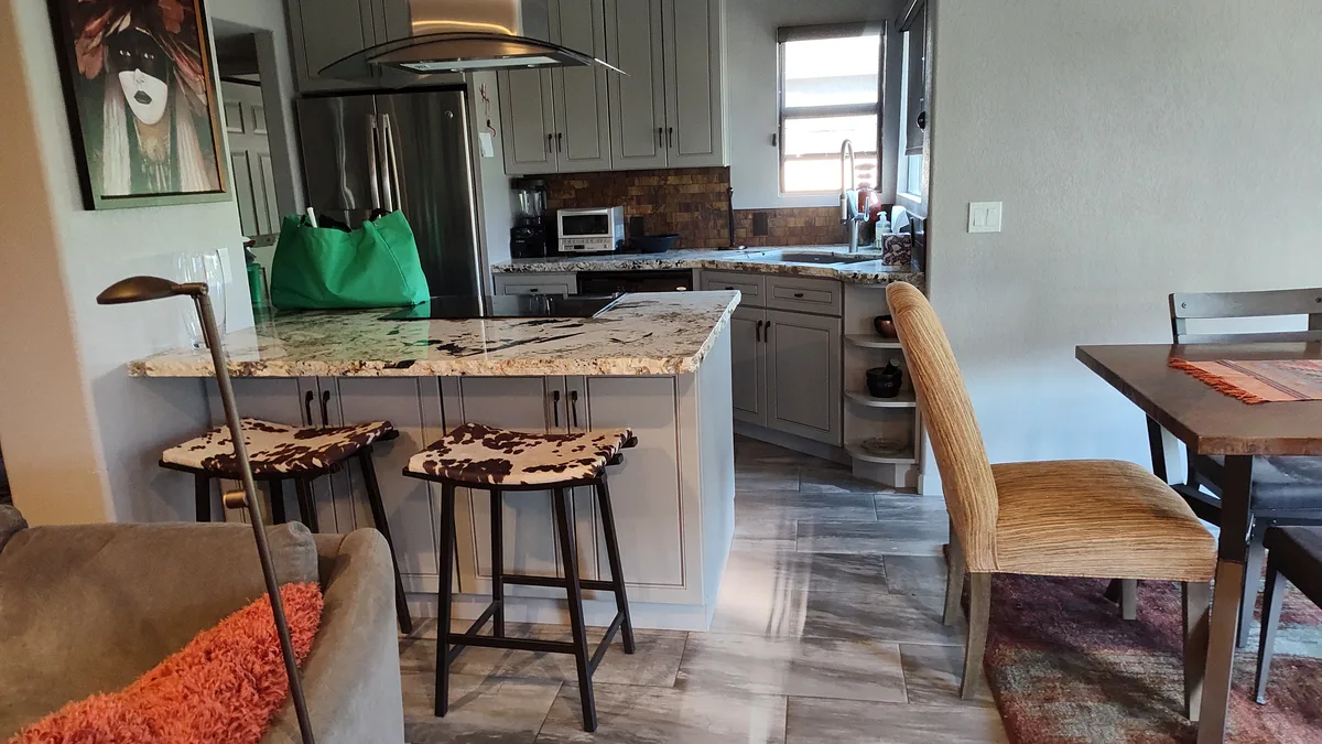 A lived-in, tidy Tucson kitchen and dining area with an island, bar stools and tile floors